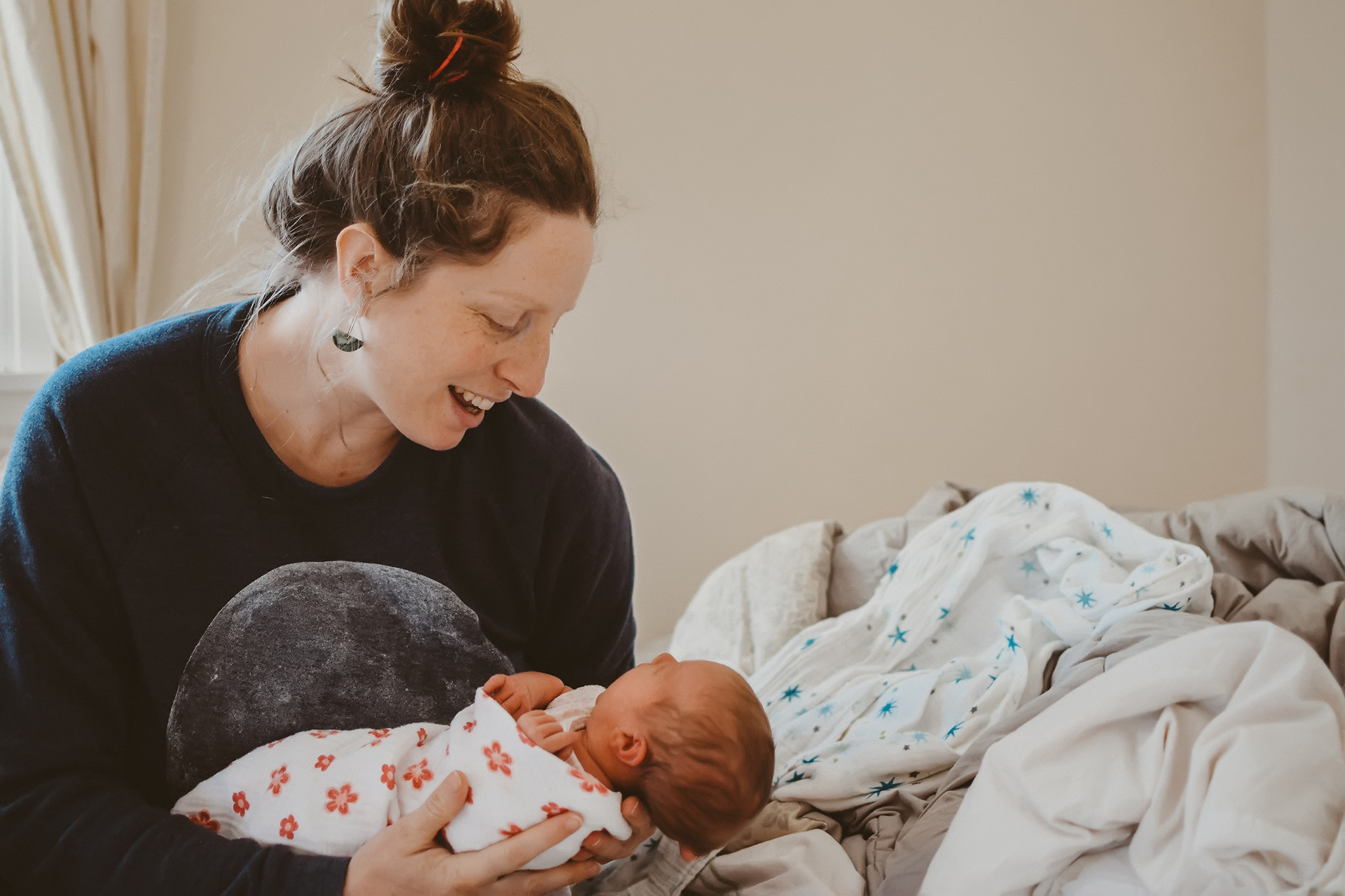 New mother smiles down at her swaddled baby, photo by Natalie Broders New mother smiles down at her swaddled baby, photo by Natalie Broders