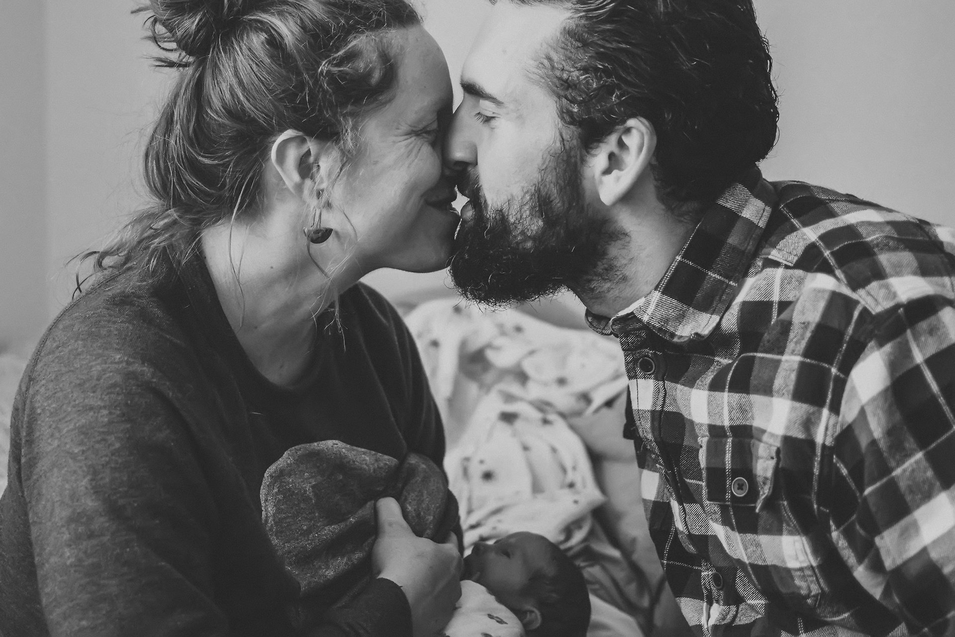 New parents kiss over their newborn baby while she breastfeeds New parents kiss over their newborn baby while she breastfeeds
