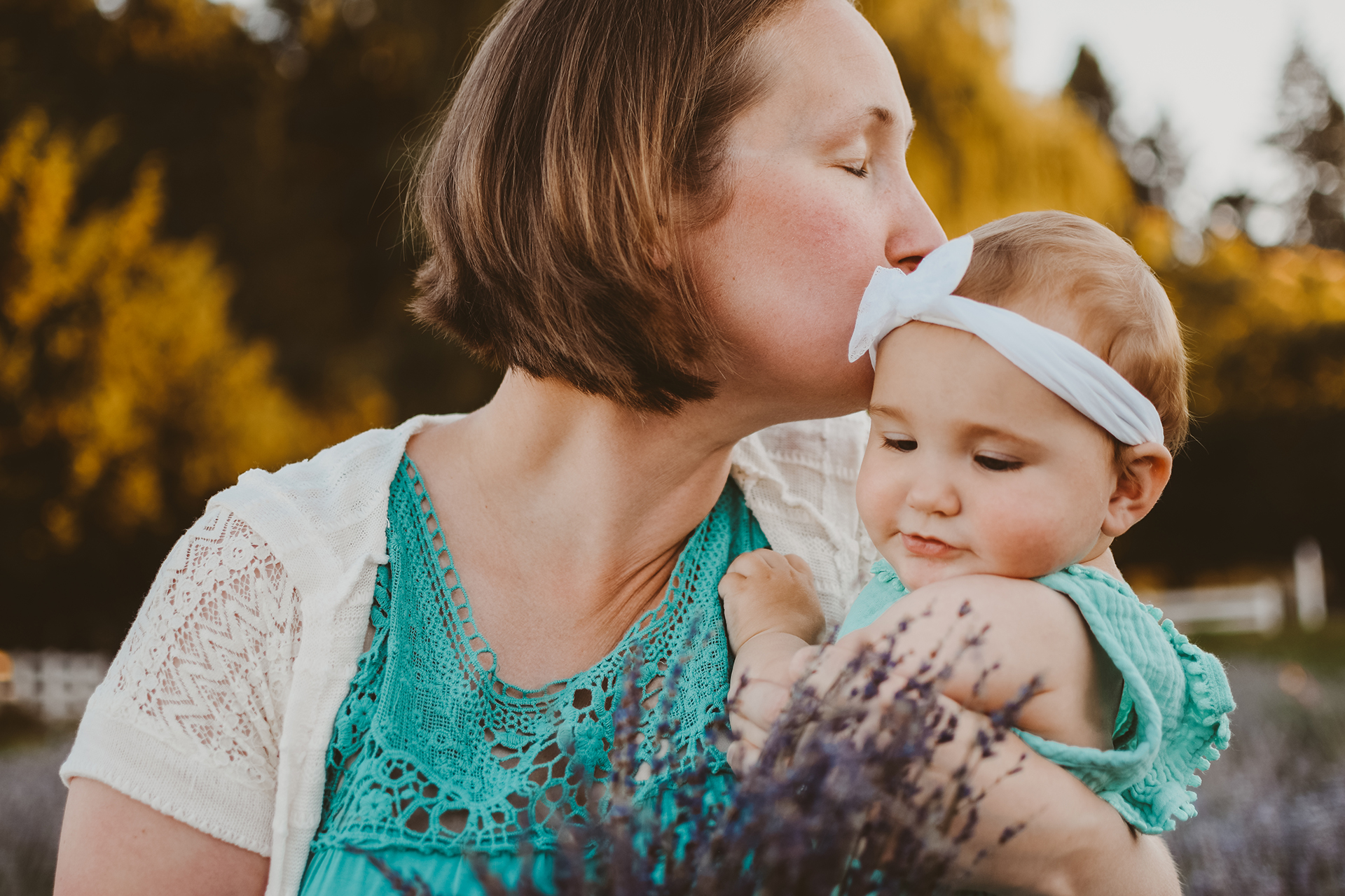 Mother kisses her infant daughter on the head while holding a bundle of lavender on Sauvie Island in Oregon Mother kisses her infant daughter on the head while holding a bundle of lavender on Sauvie Island in Oregon