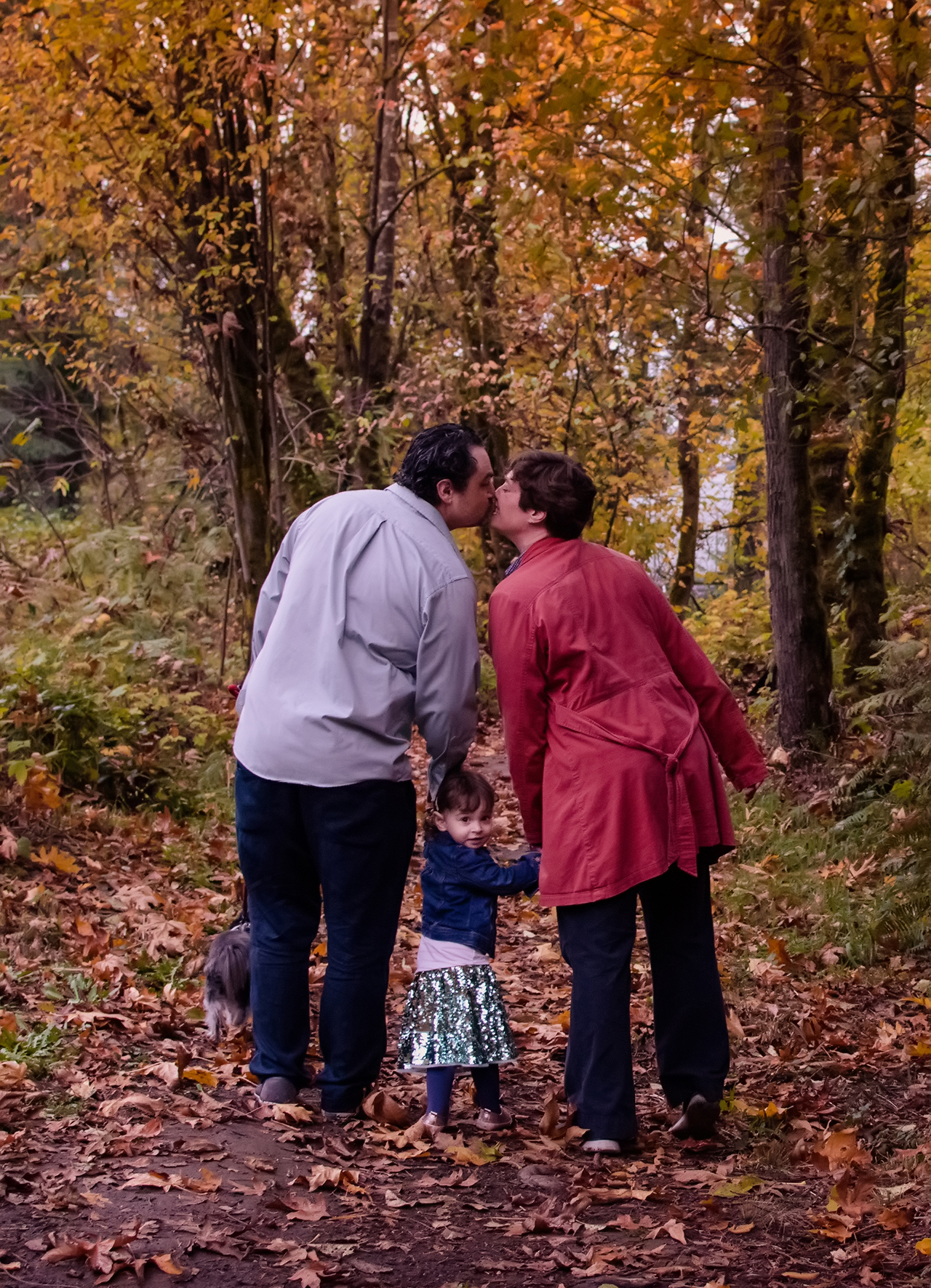 Man and wife kiss while their preschool aged daughter looks back at the camera coyly Man and wife kiss while their preschool aged daughter looks back at the camera coyly