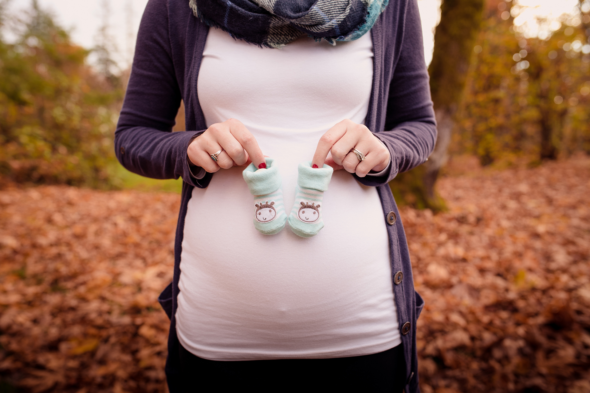 Gender reveal photo, a pregnant woman holds two tiny blue shoes among fall leaves in St Helens, OR Gender reveal photo, a pregnant woman holds two tiny blue shoes among fall leaves in St Helens, OR